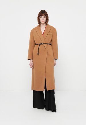 Cappotto in misto lana color cammello con colletto a punte, maniche lunghe e uno spacco frontale. Presenta una cintura nera e dettagli con tasche laterali.