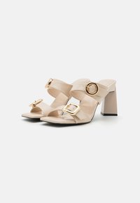 Beige Block-Absatzsandalen mit zwei breiten Riemen, die mit goldenen Schnallen versehen sind. Das Material hat eine Krokodil-Optik.