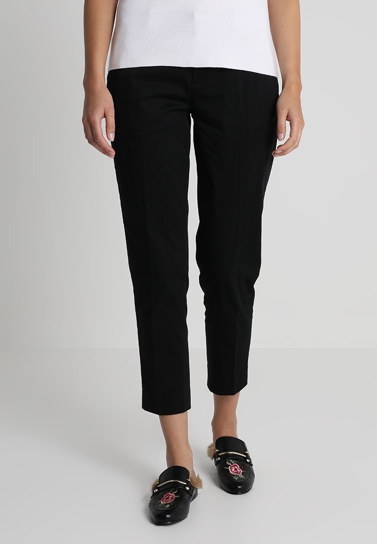 Pantalones negros, ajustados y de corte corto. Tela suave con costuras delanteras y sin bolsillos visibles. Combinados con mocasines negros.