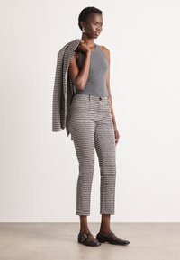 Graues Tanktop, gemusterte schwarz-weiße Caprihose und ein passender Blazer lässig über die Schulter geworfen. Schwarze Ballerinas mit goldfarbener Schnalle.
