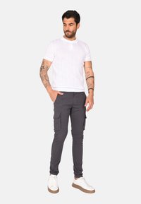 Polo shirt in maglia bianca a maniche corte con righe verticali testurizzate, abbinato a pantaloni cargo grigi scuri con tasche laterali e sneaker bianche.