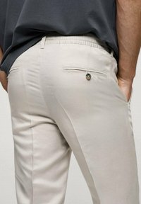 Lichtbeige broek van een zachte stof, met een elastische tailleband, achterzakken en een decoratieve knopenaccent.