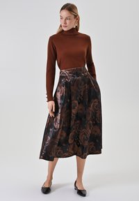 Brauner Rollkragenpullover kombiniert mit einem voluminösen, schwarzen Rock mit floralen Rosenmotiven in bronzefarbenen Tönen. Schwarze Ballerinas runden das Outfit ab.