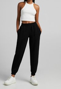 Svarta taperade byxor med elastisk midja och sidofickor, kombinerat med en vit ribbad crop top. Vita sneakers fulländar outfiten.