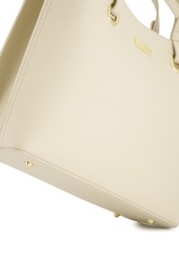Beige kožená taška s texturovaným povrchem, zlatými detaily a ochrannými nohami na spodní straně. Obsahuje kruhové úchyty.