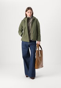 Giacca leggera verde con cappuccio. Borsa a spalla marrone, jeans a gamba larga blu e top grigio completano l'outfit. Texture liscia e design moderno.