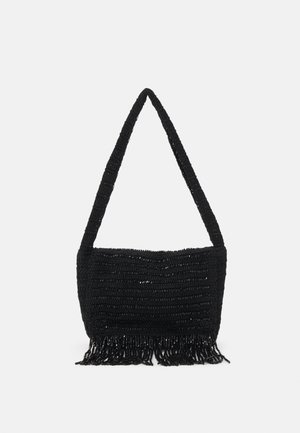 Czarna szydełkowa torba na ramię z długim paskiem i frędzlami wzdłuż dolnej krawędzi na jednolitym tle.