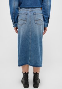 Denimkjol i ljusblått med rå kant och två bakfickor. Bärs med svarta ankelstövlar. Har en slät yta och en figurnära design.