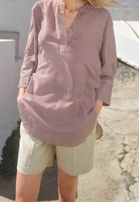 Chemise à rayures à manches longues dans des tons de bordeaux et blanc, avec un col à encoches et une coupe décontractée, associée à un short en lin beige.