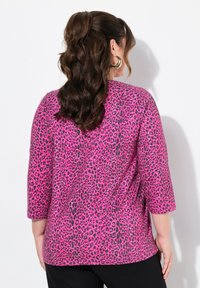 Rosa Leopardenmuster-Oberteil mit Dreiviertelärmeln, leichtem Stoff, Rundhalsausschnitt und seitlichen Schlitzen, kombiniert mit schwarzen Hosen.