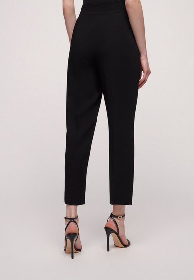 Pantalons noirs ajustés avec une coupe slim, de longueur cheville, en tissu lisse, avec des détails de couture latérale. Associés à des sandales à talons hauts noires à brides.