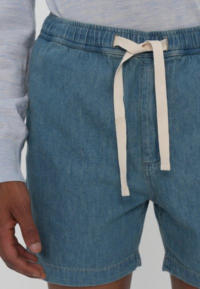 Shorts en denim bleu avec une taille élastique, un cordon blanc et un ourlet cousu. La vue en gros plan met en valeur la texture et les détails du tissu.