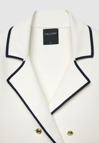 Weißer Blazer mit dunkelblauer Paspelierung am Kragen und Revers, mit zwei goldenen Knöpfen und einem schwarzen "Calliope"-Etikett in Größe Small innen.