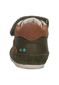 Bruine en olijfgroene sneaker van suede en textiel, met klittenbandsluiting en twee kleine turquoise stippen op de hiel. Klassiek ontwerp.