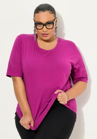 T-shirt magenta a maniche corte con scollo rotondo, tessuto morbido e spacchi laterali. Abbinato a pantaloni neri aderenti.