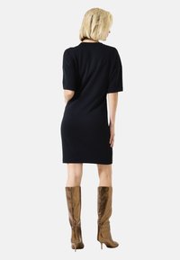 Zwart kortemouwjurk met een recht model, tot op de knie. Gecombineerd met glanzende bruine kniehoge laarzen met een naaldhak.