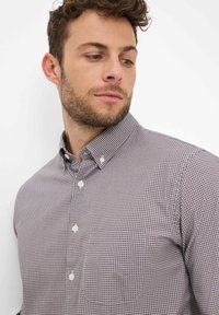 Camicia da uomo con bottoni, caratterizzata da un motivo a quadri in tonalità di bordeaux e bianco, con collo a punta e tessuto leggermente strutturato.