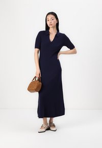 Navy ribbed knit dress with a v-neck and short sleeves. Paired with a small brown textured handbag and light-colored shoes.