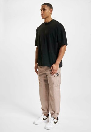 Black short-sleeve t-shirt, loose fit; paired with light beige cargo pants featuring side pockets; white sneakers with black accents.