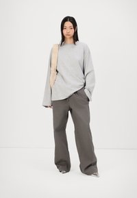 Chemise grise à manches longues avec une coupe décontractée, associée à un pantalon marron ample ; les accessoires comprennent un sac léger et texturé porté sur l'épaule.