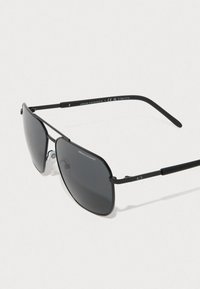 Zwarte pilotenbril met donkere glazen, metalen frame en siliconen neuspads. Gemerkt met "Armani Exchange" op het bovenste frame en de pootjes.