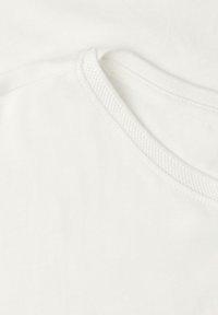Gros plan d'un T-shirt blanc en coton à col rond montrant des coutures texturées au niveau du col et une surface de tissu lisse.