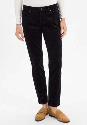Czarne spodnie sztruksowe o slim fit, z przednimi kieszeniami, zapięciem na guziki i miękką teksturą. Połączone z brązowymi mokasynami.