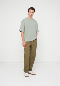 Φαρδιά μπλούζα ανοιχτού πράσινου χρώματος σε συνδυασμό με χακί παντελόνι και λευκά αθλητικά με καφέ σόλες. Απλό σχέδιο, απαλή υφή, χωρίς σχέδια.