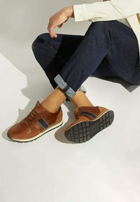 Bruine leren sportschoenen met een marineblauwe streep, getextureerde suède accenten en een witte zool. Voorzien van een vetersluiting aan de voorkant en een getextureerde zwarte rubberen zool.