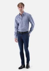 Hellblaues gemustertes Hemd mit Knöpfen und langen Ärmeln, kombiniert mit dunkelblauen Skinny-Jeans und schwarzen Lederstiefeln. Schwarzer Gürtel inklusive.