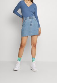 Maglietta a maniche lunghe blu con scollo a V, abbinata a una mini gonna in denim azzurro chiaro con orli sfilacciati, e sneakers bianche alte con calze colorate.