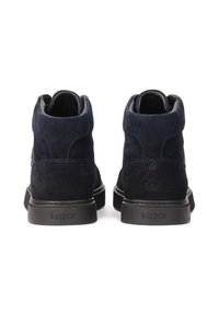 Jūras spēku zilo zamšveida potīšu zābaku teksturēta virsma ar gumijas zoli un iegravētu zīmolu uz papēža. Noapaļota silueta ar augstu apkakli.