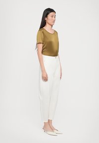 Olive satin short-sleeve top paired with white high-waisted trousers and cream slip-on shoes, featuring a smooth texture and tailored fit.