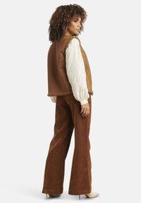 Brown suede vest with shearling trim, paired with brown corduroy wide-leg pants. White embroidered long-sleeve blouse underneath.
