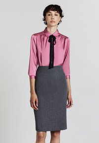 Blouse en satin rose avec un nœud papillon noir, associée à une jupe crayon grise à rayures. La blouse a un col et des manches longues.