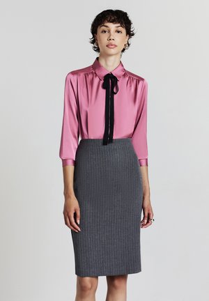 Blouse en satin rose avec un nœud papillon noir, associée à une jupe crayon grise à rayures. La blouse a un col et des manches longues.