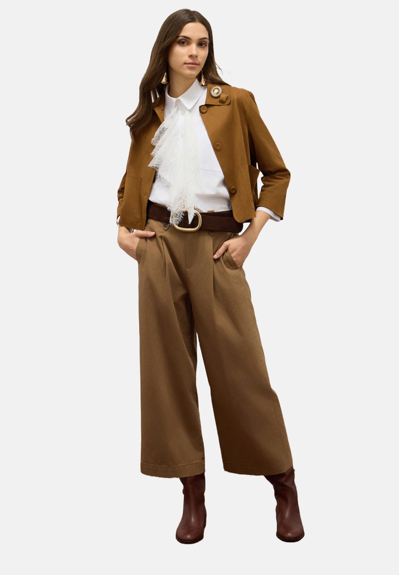 Bordeaux cropped jack met een ronde knop, witte blouse met kantdetails, bordeaux wijde broek en bordeaux haklaarzen.