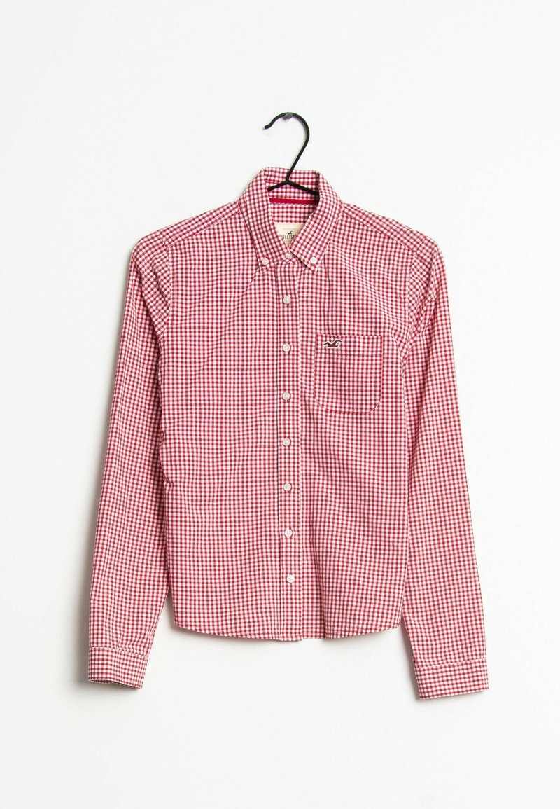 Chemise à carreaux rouge et blanc accrochée à un crochet, avec des manches longues, une poche poitrine gauche et un col classique. Tissu en mélange de coton.