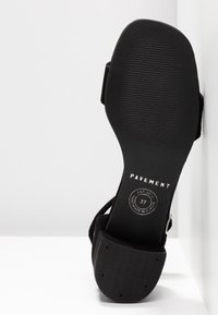 Sandale à talons noirs avec semelle texturée, dotée d'une bride ajustable à la cheville et d'un logo estampillé sur la semelle intérieure. Taille 37.