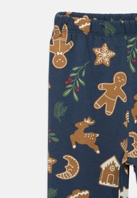 Καλσόν από βαμβάκι με σκοτεινό μπλε φόντο, που διαθέτει εορταστικούς άνδρες από τζίντζερ, τάρανδους, αστέρια και μοτίβα εορταστικών φυτών σε καφέ και πράσινο χρώμα.