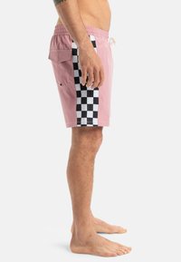 Pantalones de baño rosa con panel lateral a cuadros en blanco y negro, cinturilla elástica y bolsillo con abertura en el lateral. Textura de tela suave.