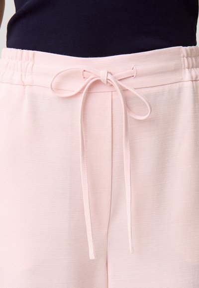 Section taille d'un pantalon rose clair avec un cordon de serrage noué et une taille élastique, porté avec un haut foncé.