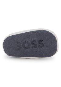 Semelle d'une chaussure avec une surface texturée de couleur gris foncé, portant le mot "BOSS" en relief. Les bords sont arrondis et le design est minimaliste.
