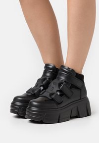 Tjocka svarta sneakers i läder med kardborreband, en vadderad krage och en tjock, strukturerad platåsål.