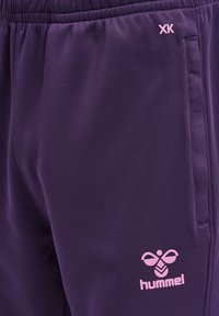 Short de sport violet avec poches latérales, taille élastique, logo "hummel" rose et motif d'abeille sur la cuisse droite.