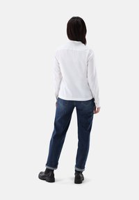 Weißes Langarmhemd mit Kragen, kombiniert mit locker geschnittenen dunkelblauen Jeans und schwarzen Ankle Boots, von hinten betrachtet.