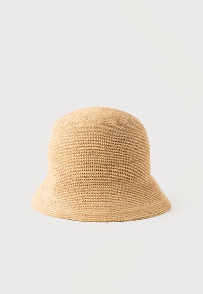 Μπεζ υφασμάτινο καπέλο τύπου κάδος με γείσο που κλίνει προς τα κάτω, εμφανιζόμενο πάνω σε απλό ανοιχτό φόντο.