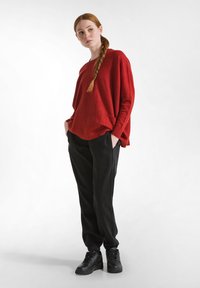 Roter übergroßer Pullover mit rundem Halsausschnitt und Seitentaschen, kombiniert mit schwarzen, schmal zulaufenden Jogginghosen mit elastischen Bündchen und seitlichen Nähten.