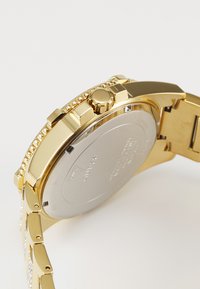 Ceas de mână cu tonuri de aur, cu un carcasă netedă, formă rotundă, bezel texturat și spate argintiu. Dispune de o brățară cu linkuri, cu accente clare pe unele link-uri.
