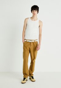 Canotta bianca a coste, pantaloni cargo beige con passanti per cintura, cintura bianca e sneakers gialle con lacci neri. Look semplice e casual.